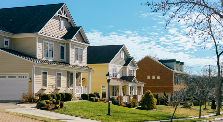 houses with front porches lining a suburban street against a blue sky with some cloud cover