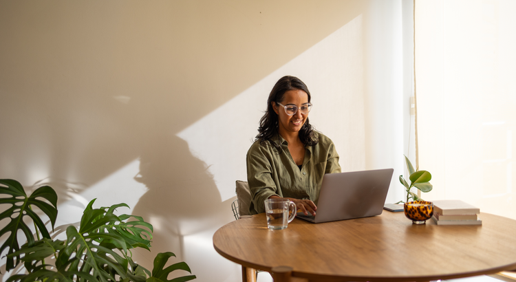 Young woman sitting at a round wooden table looking at a laptop computer