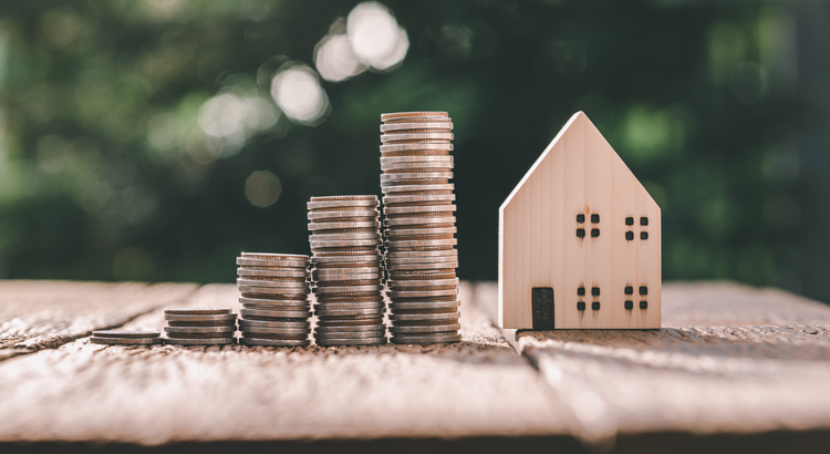 five stacks of coins in increasing amounts next to a wooden toy house on a wooden table