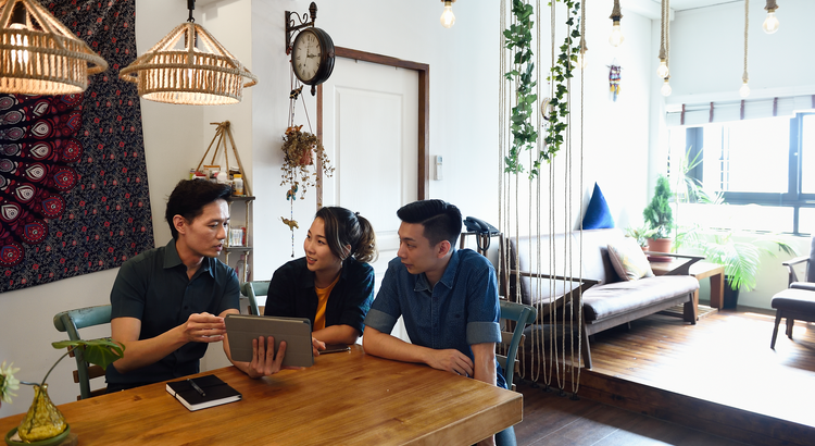 realtor showing millennial couple information on a tablet seated at a dining table in an apartment