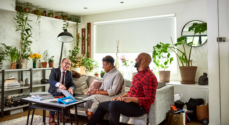 middle aged couple smiling while talking to a business man in their living room